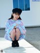 A woman sitting on a sidewalk wearing a tie dye sweatshirt and a black beret.