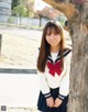 A young woman in a school uniform leaning against a tree.