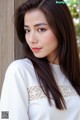 A woman with long brown hair leaning against a wooden wall.