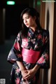 A woman in a black and pink kimono leaning against a wall.