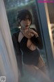 A woman in a black bodysuit leaning against a window.