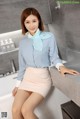 A woman in a blue shirt and pink skirt posing in a bathroom.