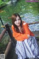 A young woman sitting on a wooden bench by a river.