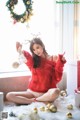 A woman in a red sweater sitting on the floor next to a Christmas wreath.