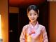 A woman in a pink hanbok standing in front of a door.