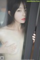 A naked asian woman looking out of a window.