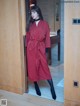 A woman standing in front of a wooden door wearing a red coat.