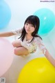 A young woman sitting on the floor surrounded by colorful balloons.