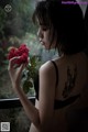 A woman holding a red rose in front of a window.