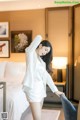 a woman in a white suit standing next to a bed