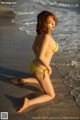 A woman in a yellow bikini sitting on the beach.