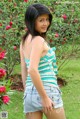 A young woman standing in front of a bush of flowers.