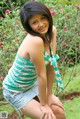 A young woman sitting on the ground in front of a bush.