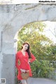 A woman in a red polka dot dress leaning against a stone wall.