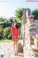 A woman in a red polka dot dress standing in front of a stone wall.