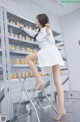 A woman in a white lab coat standing on a ladder.