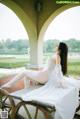 A woman in a white dress sitting on a wooden bench.