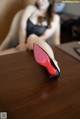 A woman sitting at a table with a pair of red shoes on it.