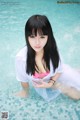 A woman in a white shirt and pink bikini sitting in a pool.