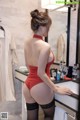 A woman in a red bodysuit and black stockings standing in front of a mirror.