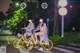 A couple of women riding on the back of a yellow bike.