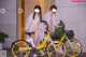 A couple of naked women standing next to a yellow bike.