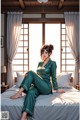 A woman sitting on a bed in a green pajamas.