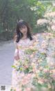 A woman in a floral dress standing in front of flowers.