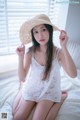 A woman sitting on a bed wearing a straw hat.