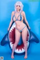 A woman in a blue bikini sitting on an inflatable shark.