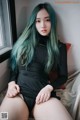 A woman with long green hair sitting on a bed.