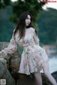 A woman in a pink dress posing on a rock by the water.