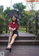 A woman in a red shirt and black skirt sitting on a wooden deck.