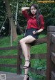 A woman in a red shirt and black skirt sitting on a wooden bridge.