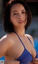 A woman in a blue bikini standing next to a pool.