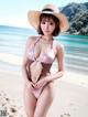 A woman in a bikini and hat on the beach.