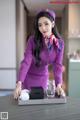 A woman in a purple uniform holding a tray with a glass of water.